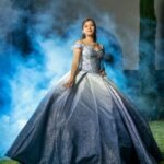 Captured moment of a young woman in a stunning blue quinceañera gown outdoors, exuding elegance and youth.