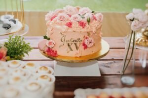 Elegant pink quinceañera cake adorned with roses and a 'XV' topper, perfect for celebrations.